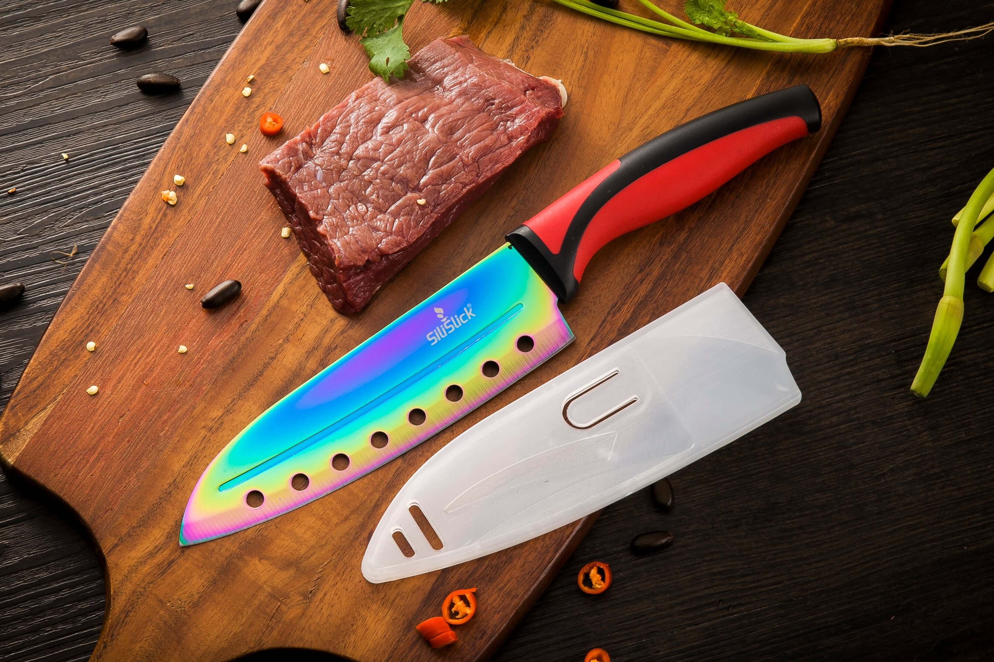 Chef's knife with a colorful blade on a wooden cutting board with raw meat.
